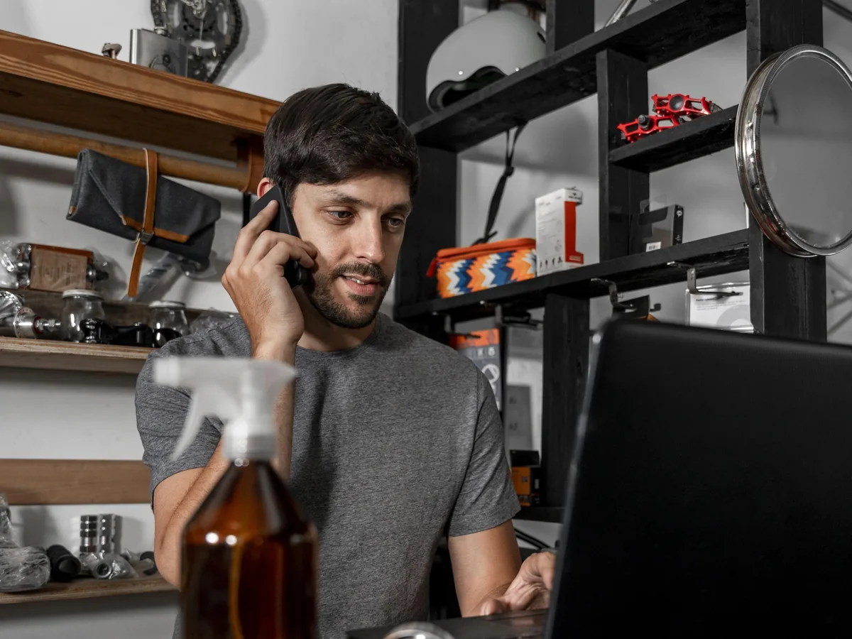 A local business owner taking a customer call while working at a laptop in their shop